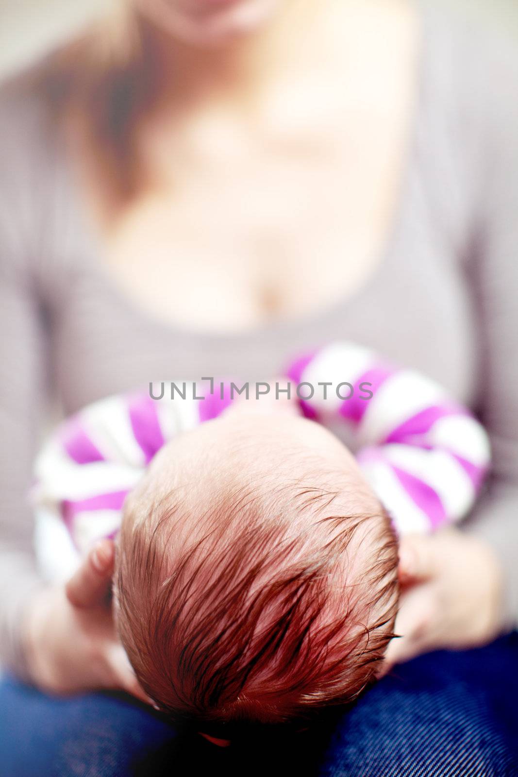 View from the top of the head of a young mother cradling her newborn baby in her hands as it rests on her lap