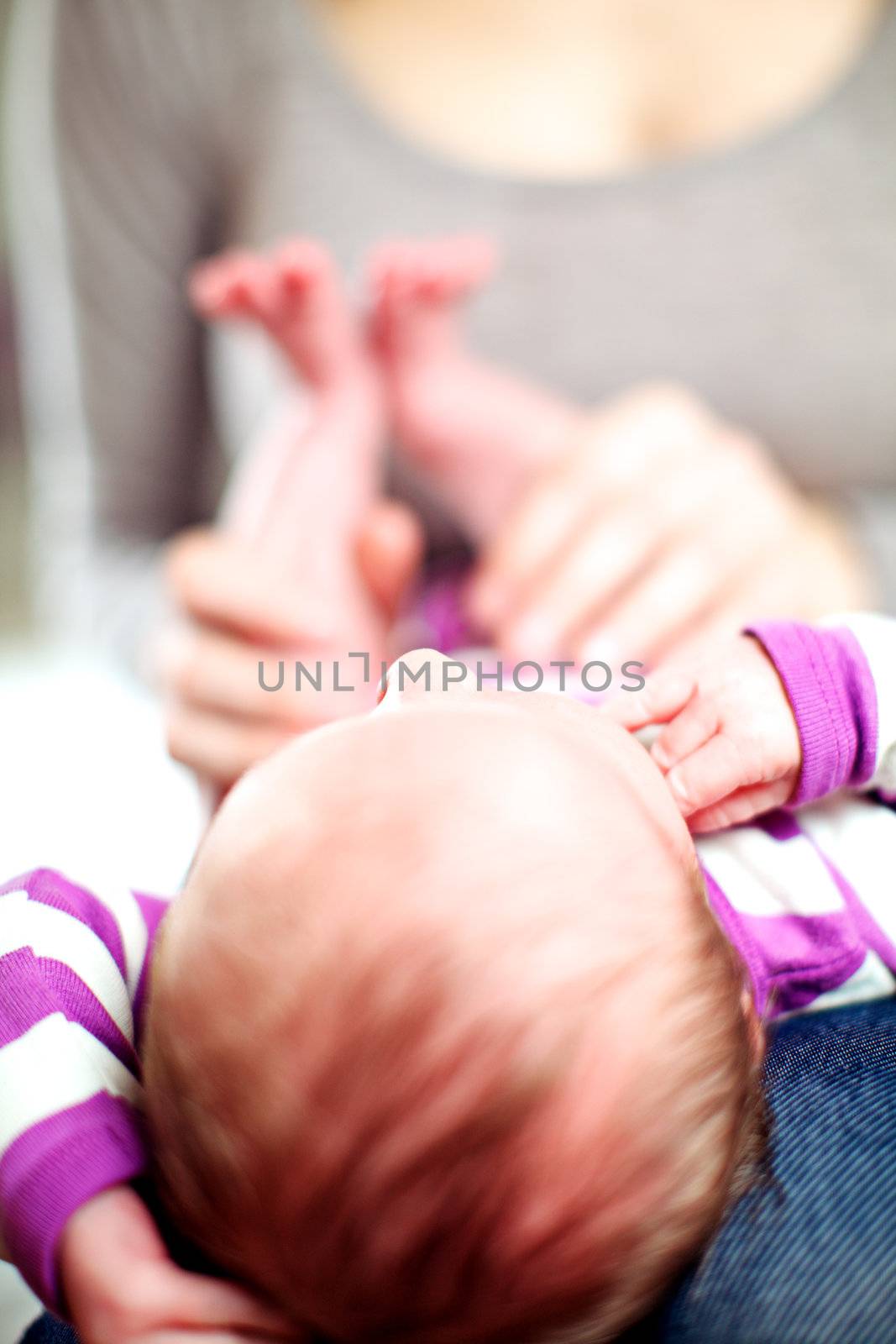 Tiny newborn baby lying on its mothers lap with its head towards the camera with shallow dof