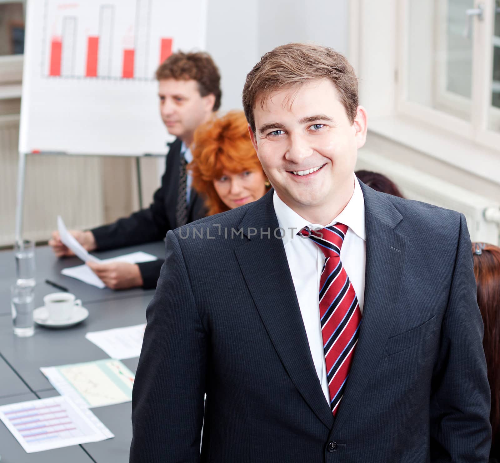 successful business smiling man portrait at office with team in background