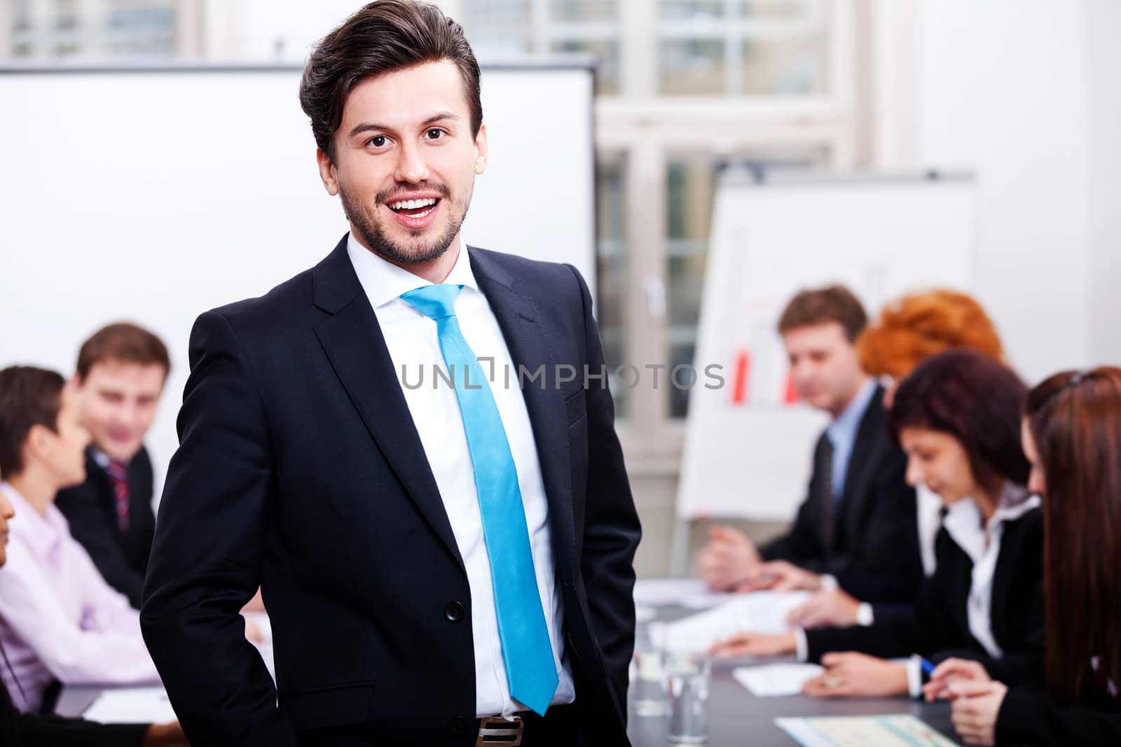 successful business smiling man portrait at office with team in background