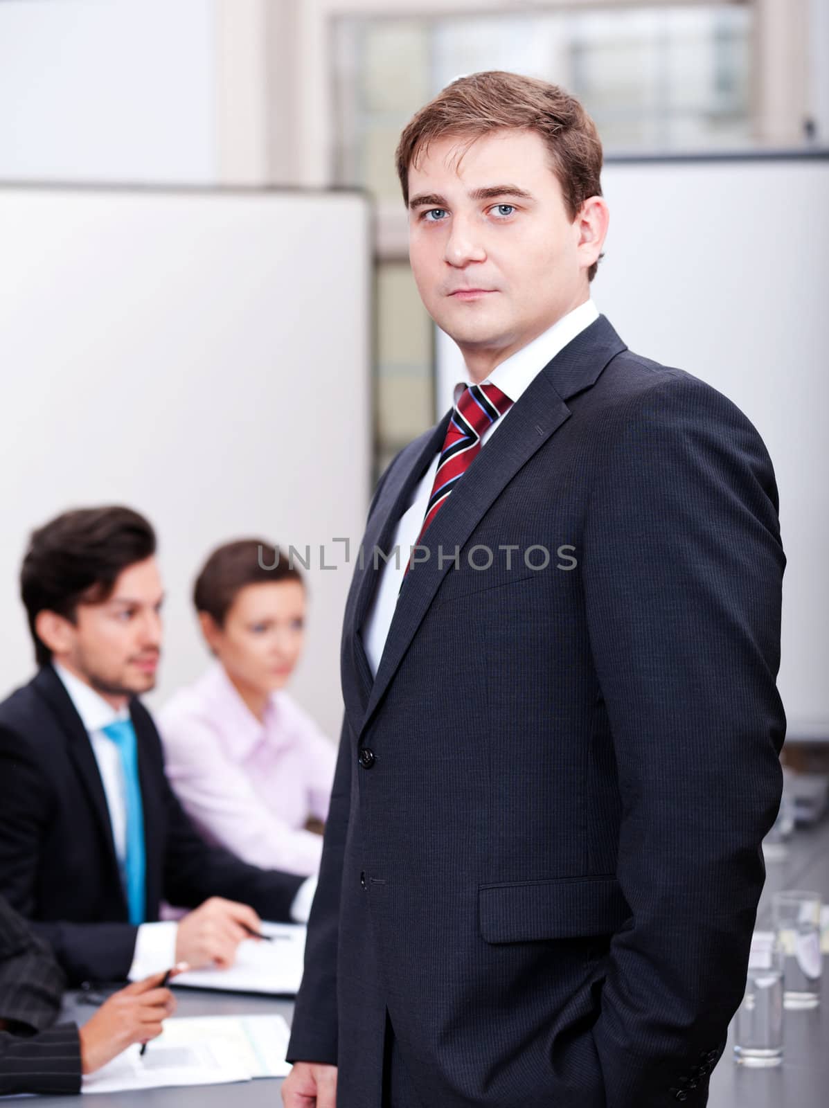 successful business smiling man portrait at office with team in background