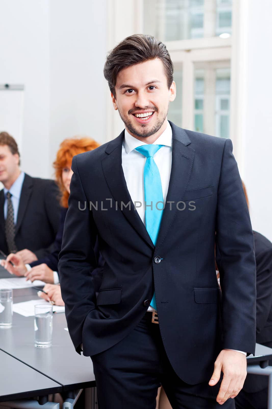 successful business smiling man portrait at office with team in background