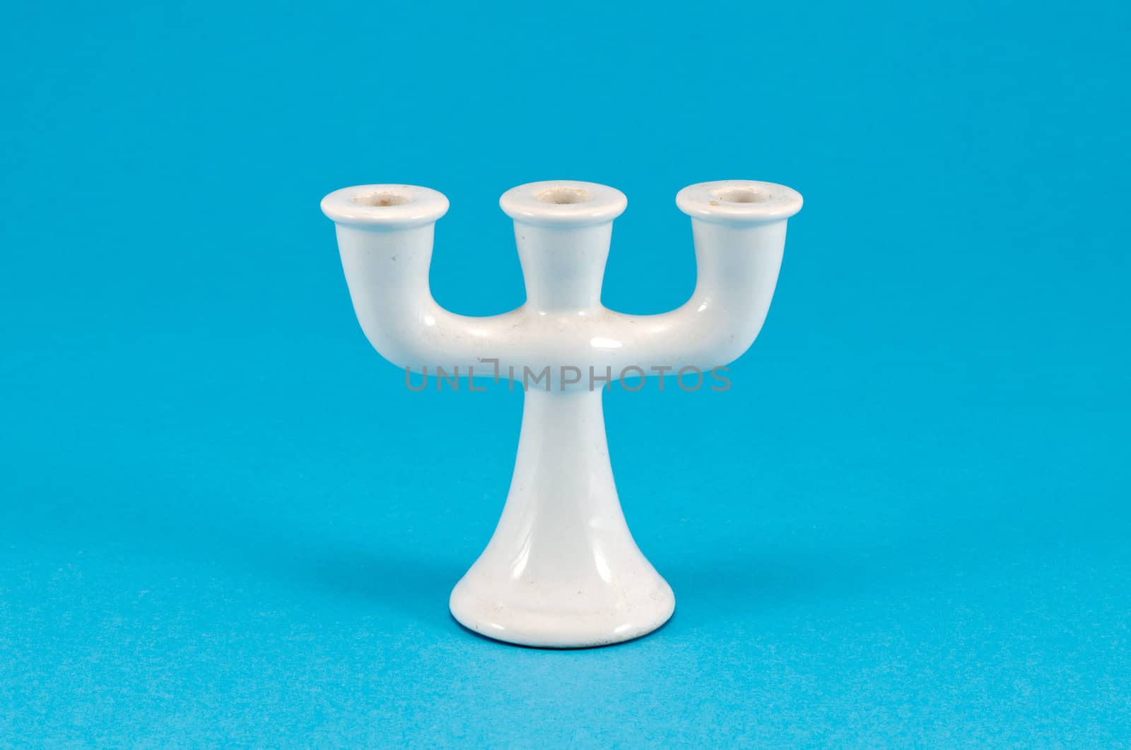 old retro ceramic white candlestick with three places for candle covered with dus on blue background.