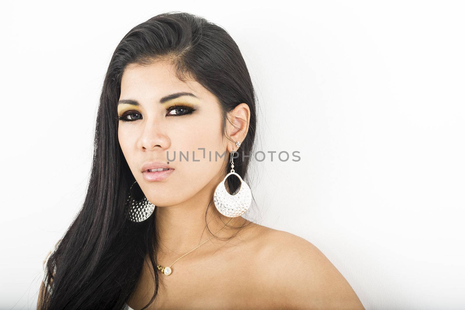 Sexy young Asian woman wearing large dangling earrings looking at the camera with a sultry look, studio portrait with copyspace