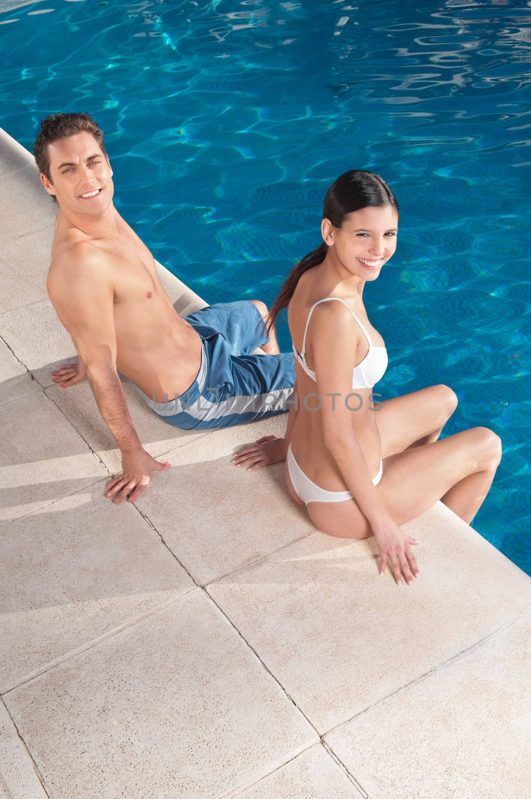 An attractive young smiling couple relaxing by the pool