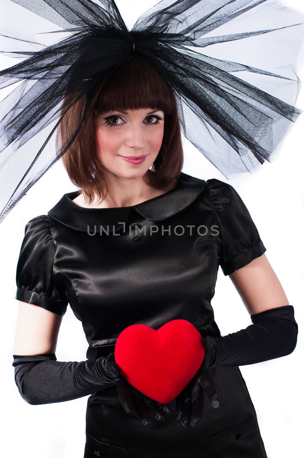 Pretty girl in black dress and big bow with red heart in her hands isolated on white background