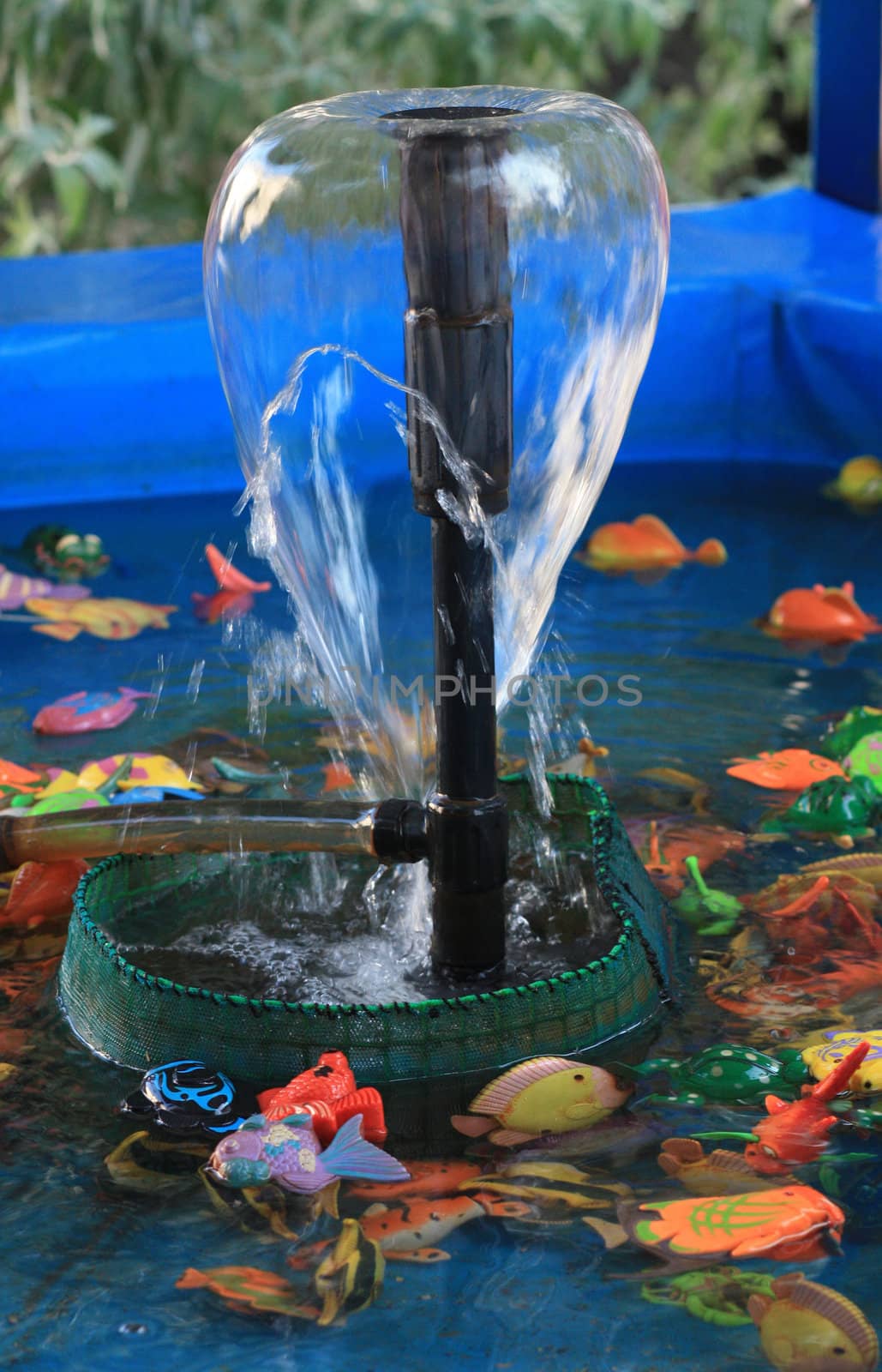 Garden fountain in a blue swimming pool with children's plastic fish