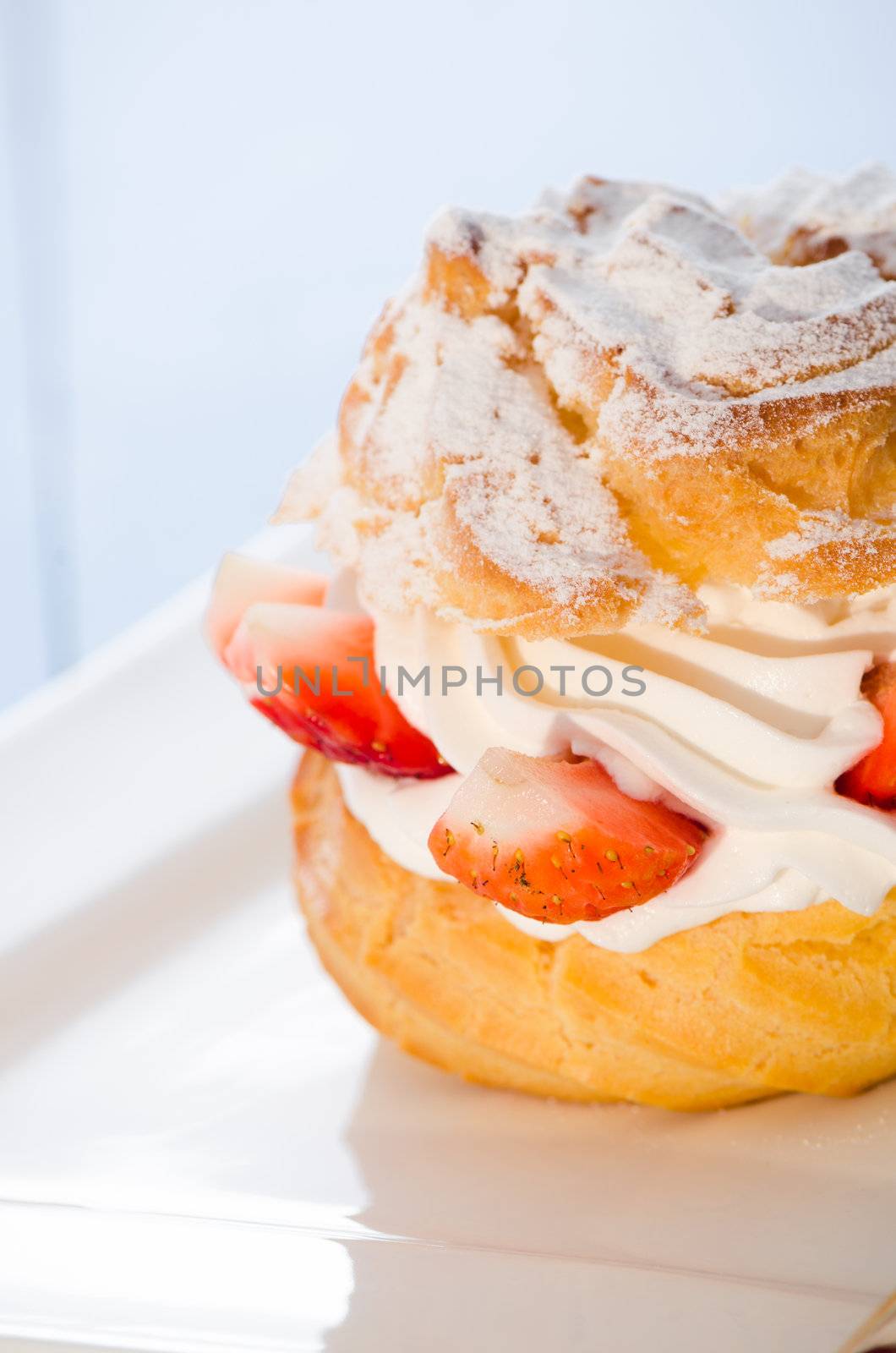 fresh cream puff with whipped cream and strawberries on white plate and light blue wood table