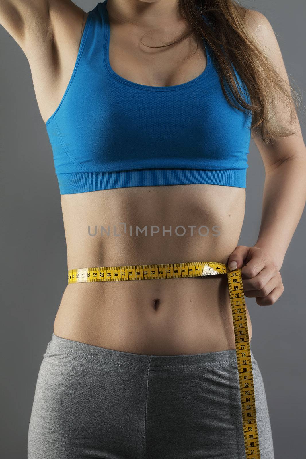 closeup of a woman measuring her waist on gray background