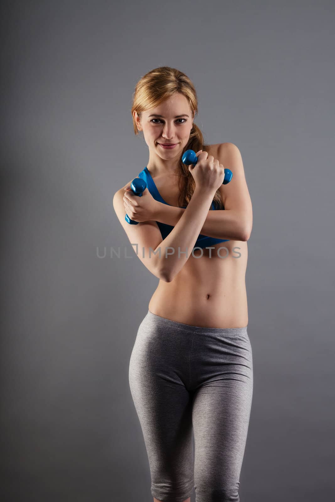 beautiful fitness woman with dumbbells on gray background