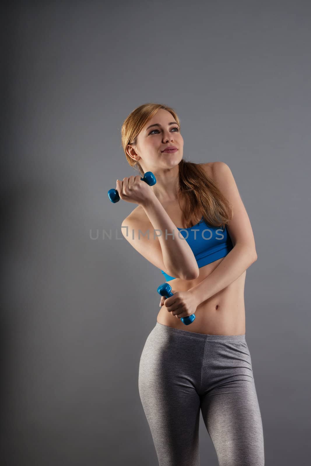 pretty fitness woman with dumbbells on gray background