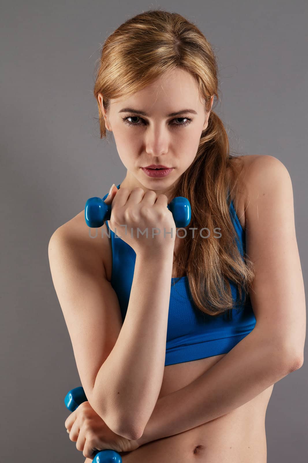 pretty fitness woman with blue dumbbells on gray background