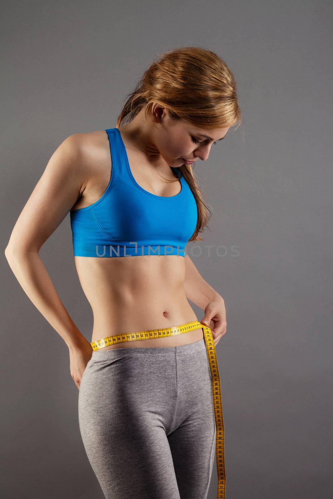 blonde fitness woman measuring her waist on gray background