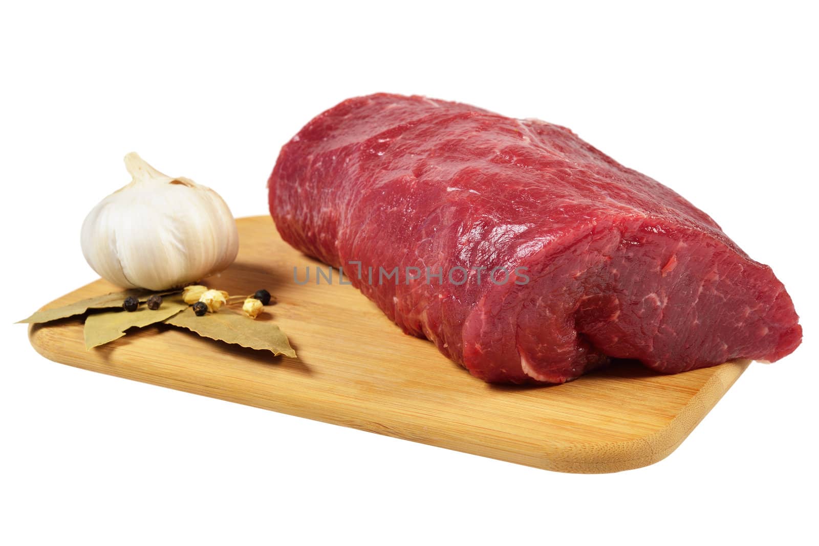 Piece of raw beef on a wooden board, decorated with garlic and bay leaves.