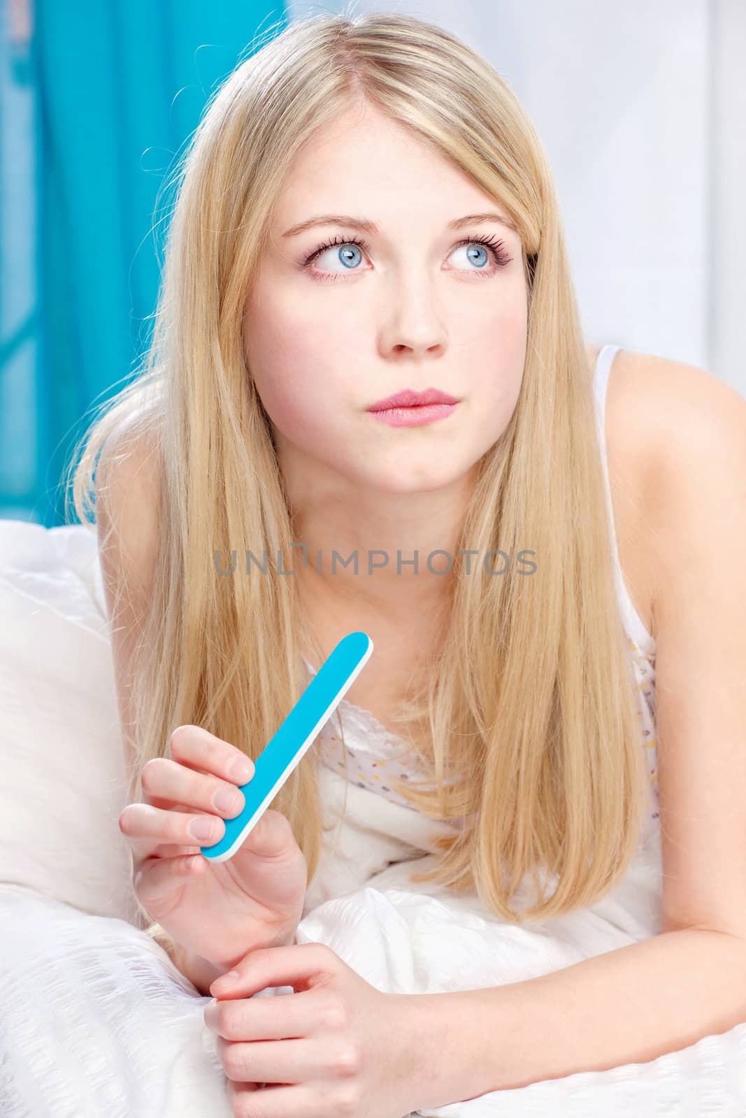 Portrait of beautiful young woman with nail file in bedroom