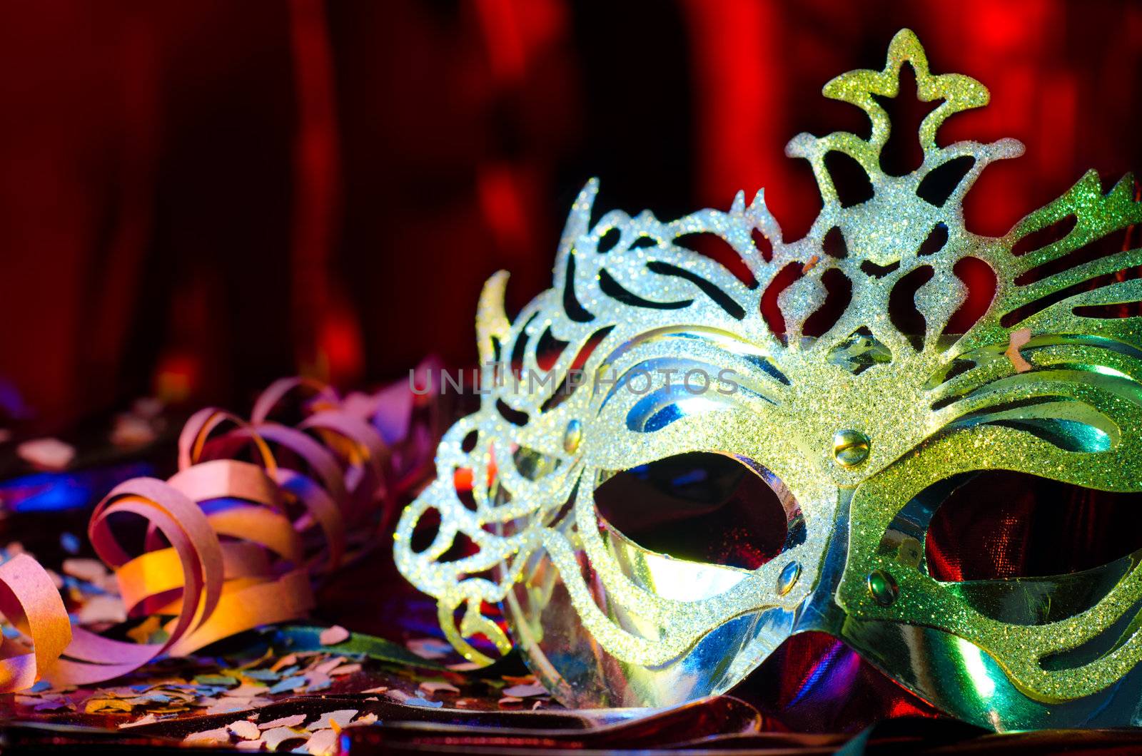 Carnival mask with a red silky background and confetis and streams on the table.