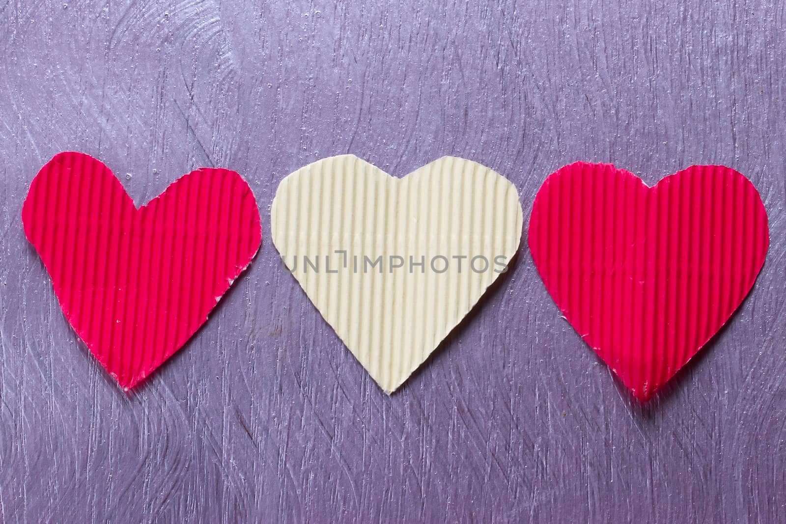 Three paper hearts red and white on the purple board