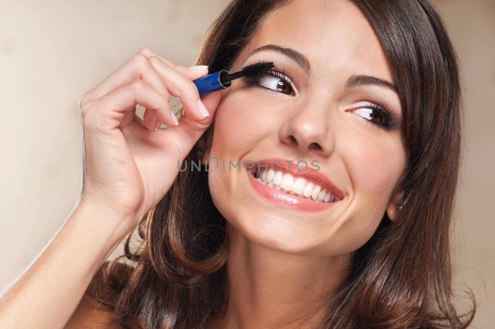 Beautiful smiling woman applying mascara on her eyelashes