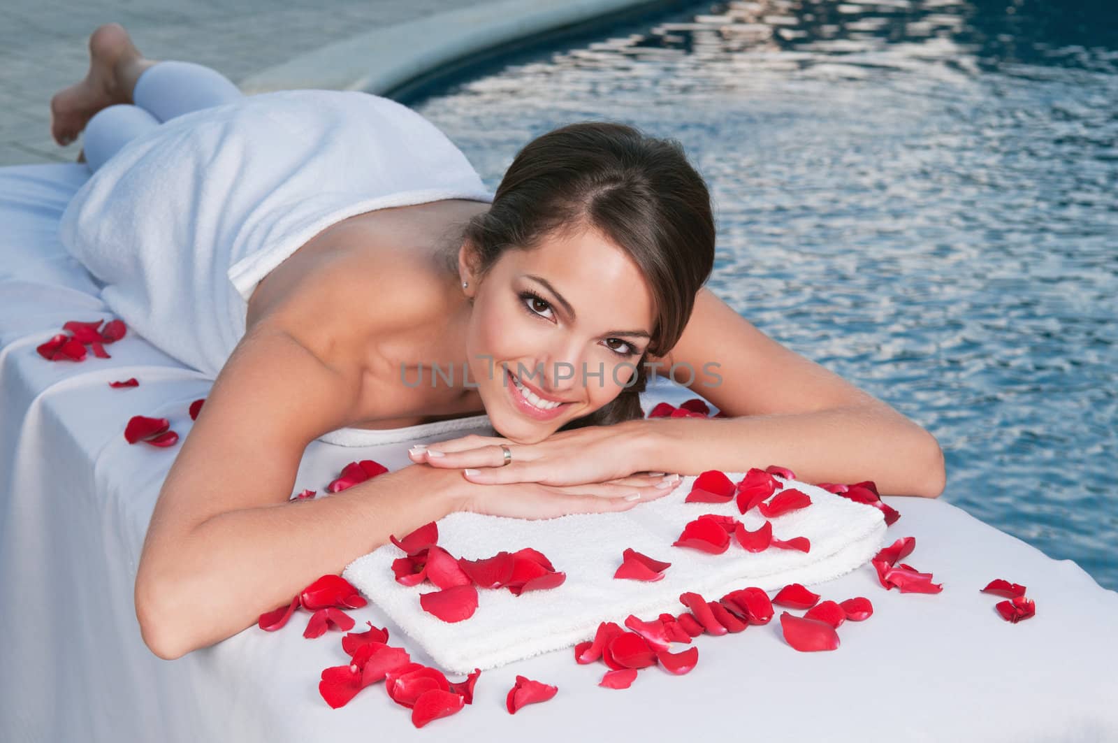 Smiling young woman at spa with rose petals around by leaf