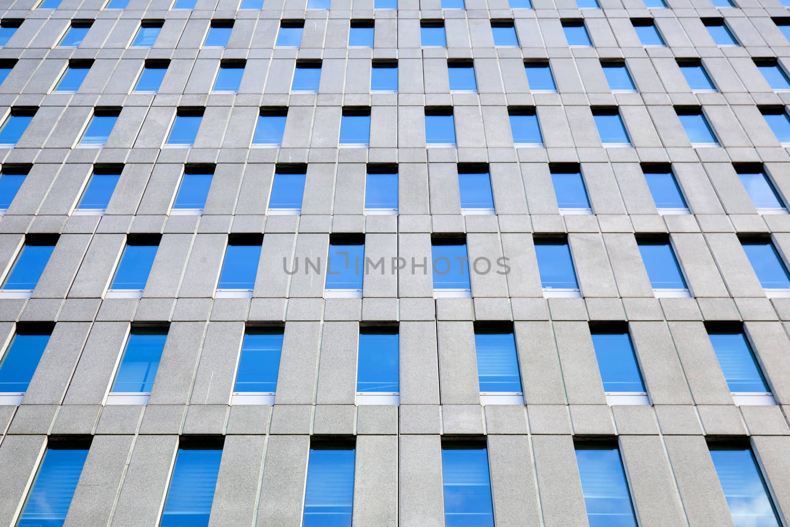 concrete facade of office building with windows reflecting blue  by ahavelaar