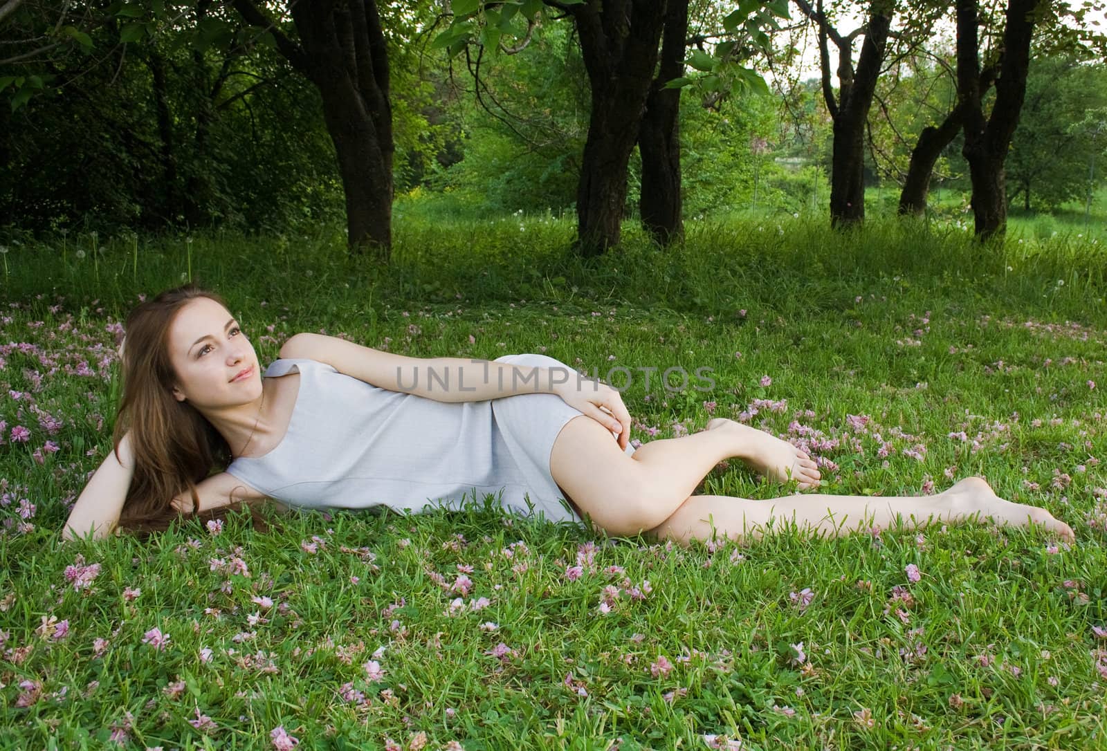 Young cute girl is leaning on the green grass and looks at the sky