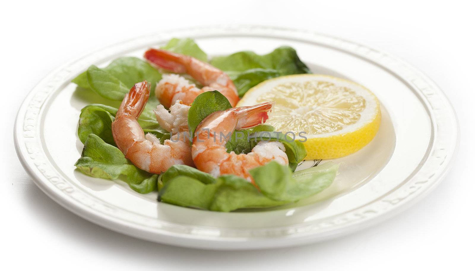 Three shrimp's tails with leek, lettuce and lemon on the white plate