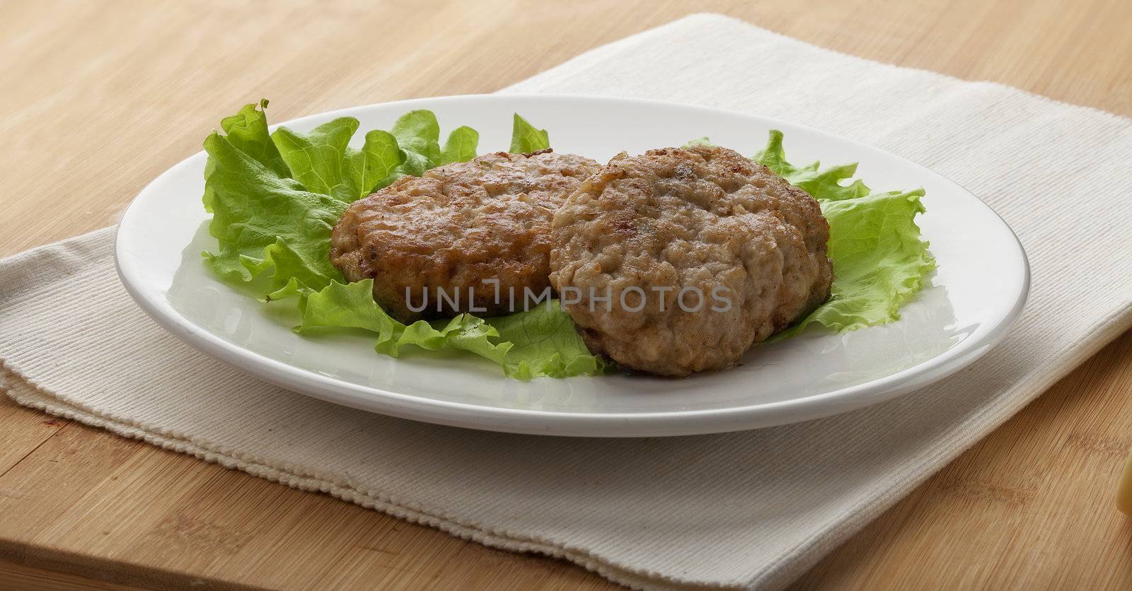 White plate with two rissoles and green lettuce on the napkin on the wooden board