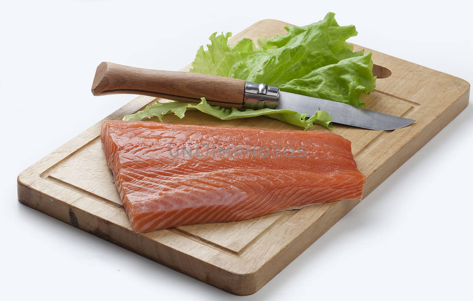 Chunk of raw salmon's fillet with knife and lettuce on the wooden board