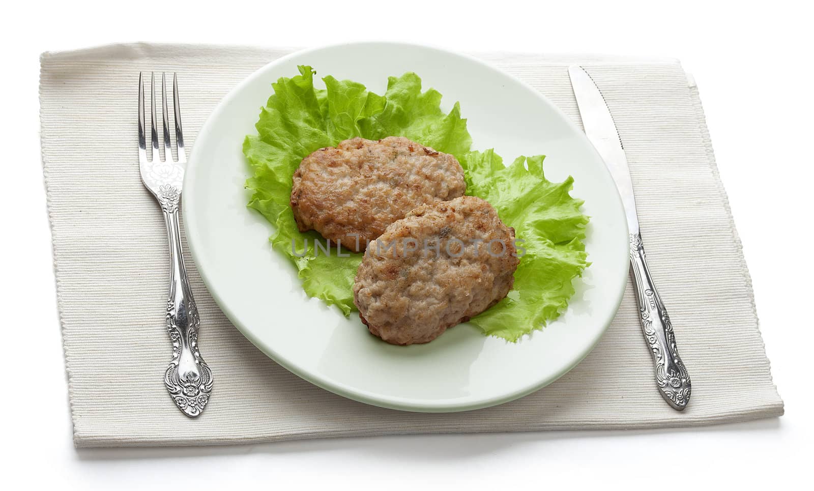 White plate with two rissoles and lettuce on the napkin with fork and knife