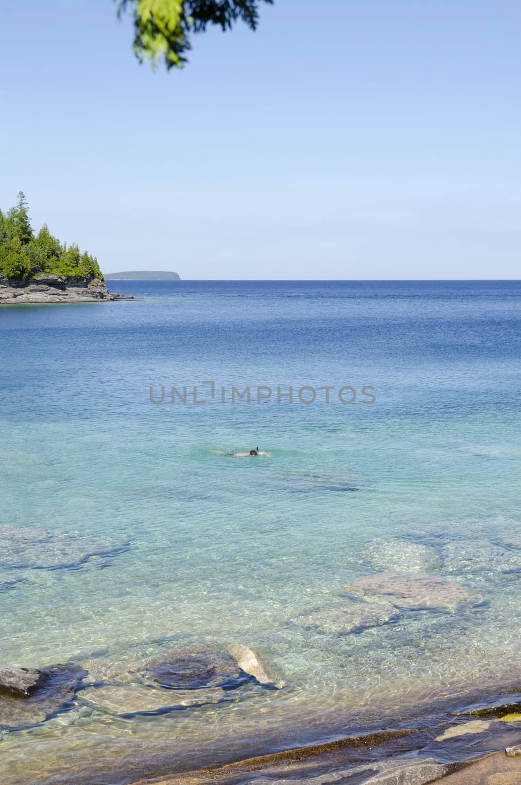 Green and blue water of Huron Lake, Ontario under blue sky.