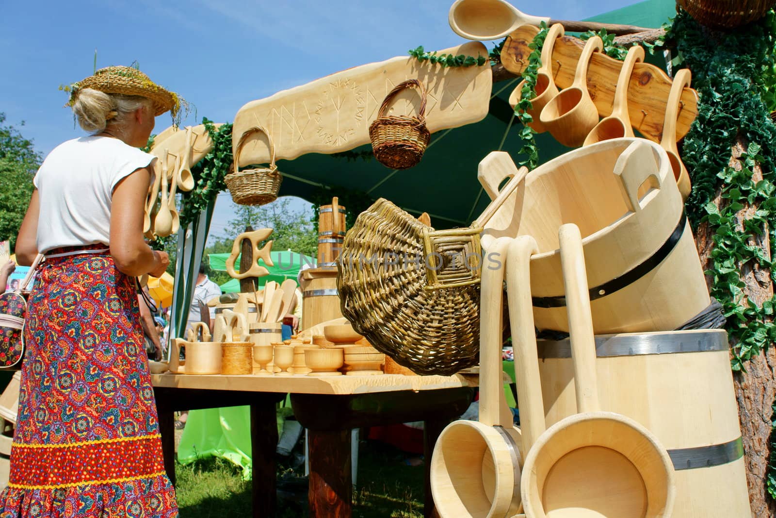 A woman buys souvenirs made of cedar stand on table of a sunny day at the street.