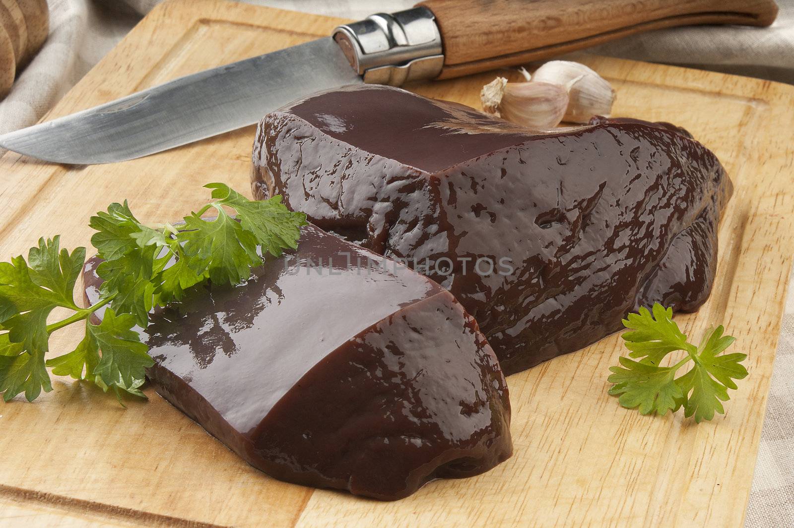 Two pieces of raw liver with parsley; garlic and knife on the wooden board