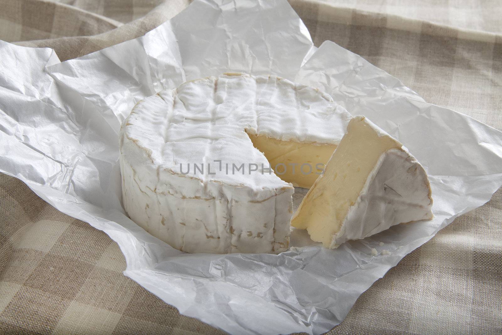 Camembert cheese in the white paper on the tablecloth