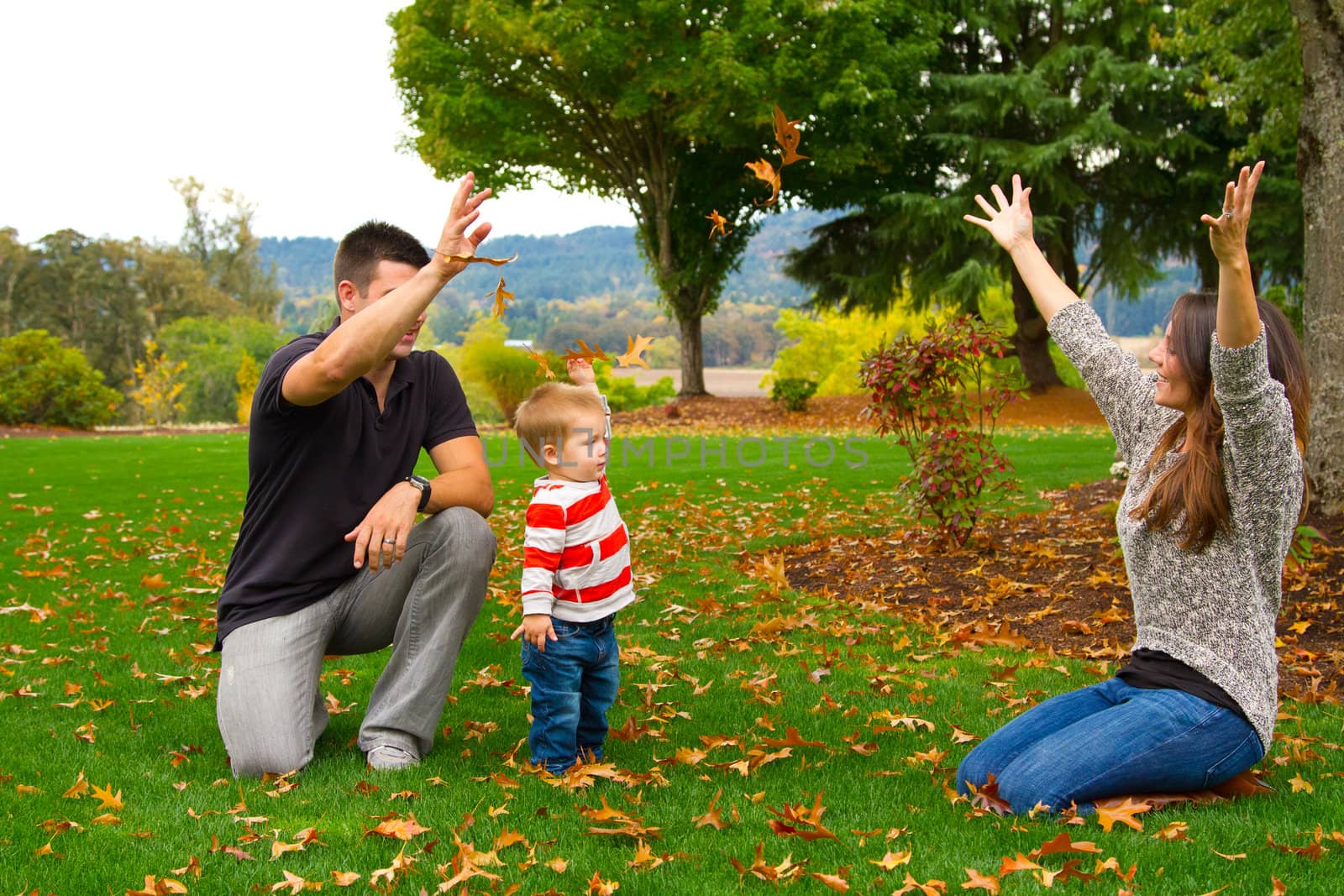 A family of three people play with leaves in the fall on a ranch.