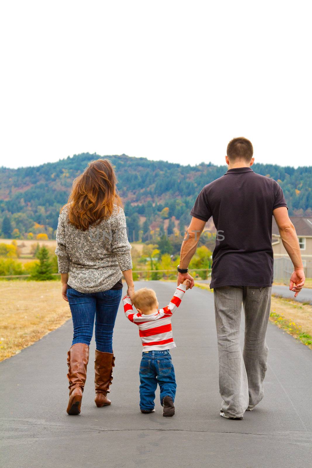 A family walks away on a path while holding hands with the child in the middle.