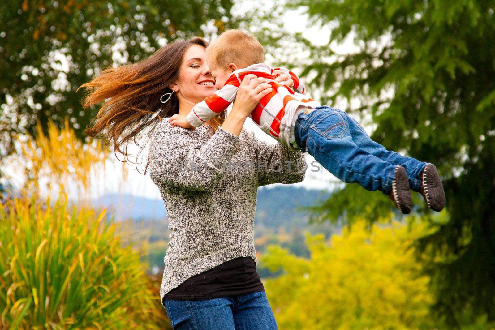 A woman spins her child around while holding him in the air in this joyous happy moment.