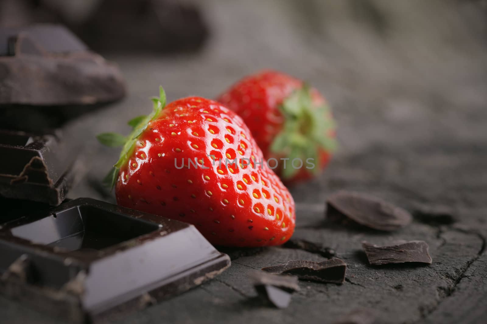 Fresh strawberries and chocolate pieces on old wood background