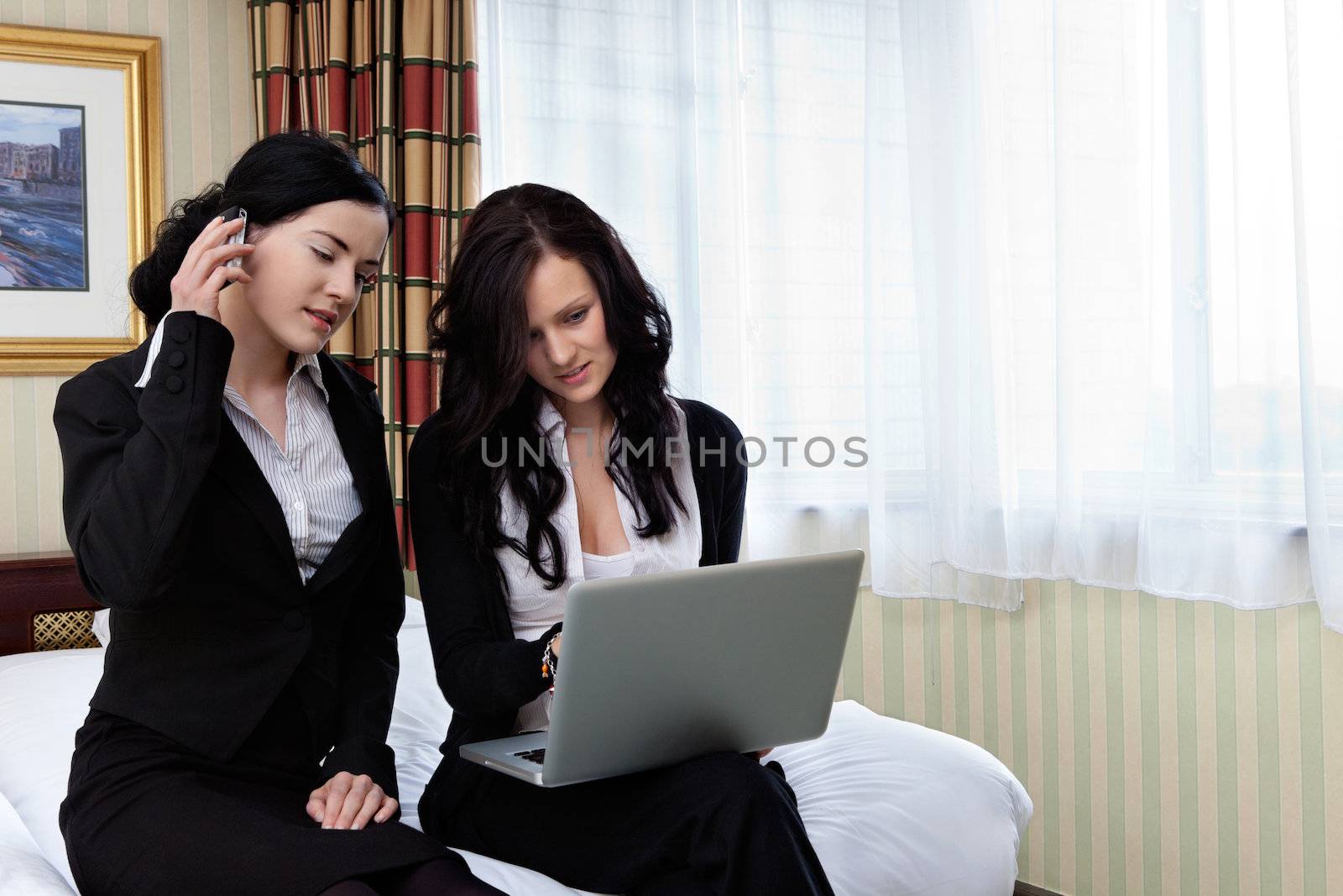 Female executive working on laptop while her colleague talks on cell phone