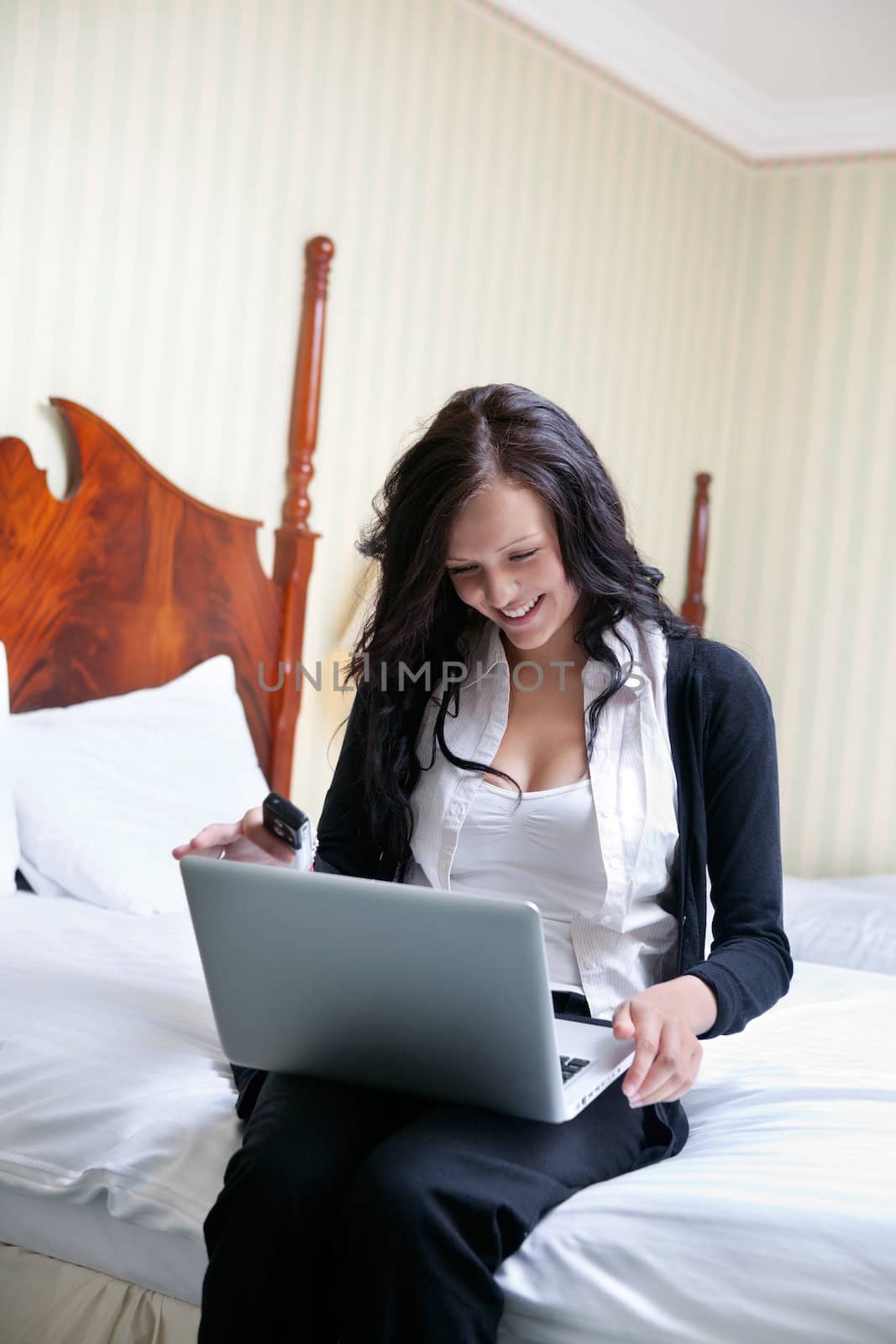 Young smiling businesswoman using laptop while sitting on bed