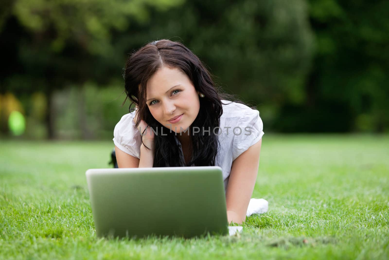 Portrait of pretty female lying down on grass with laptop