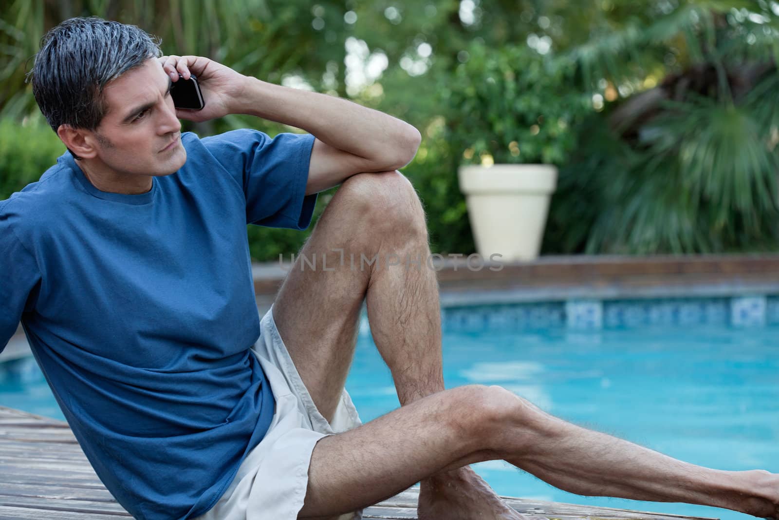 Casual man sitting near poolside talking on cell phone