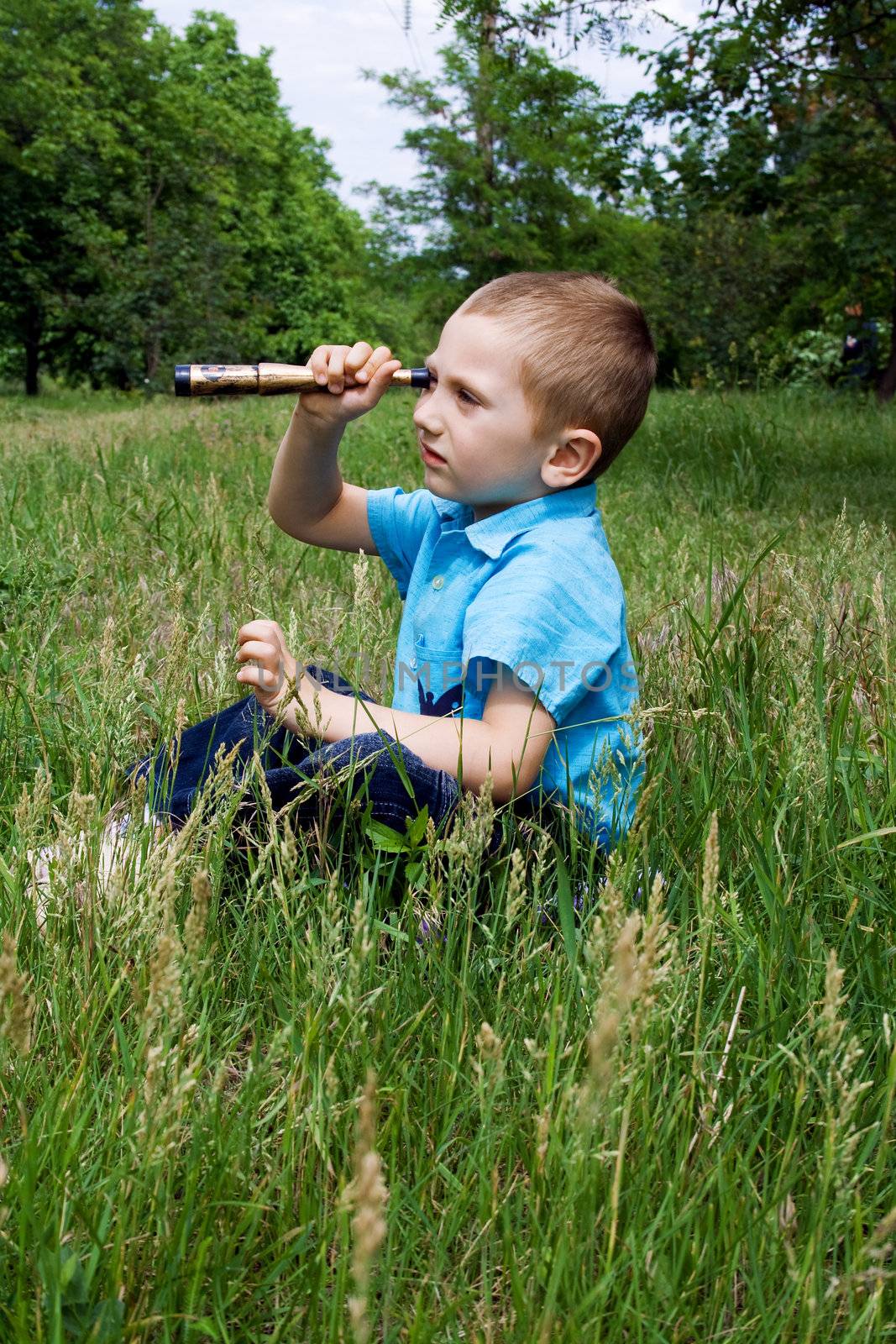 little boy sits on the green grass and playing with a toy