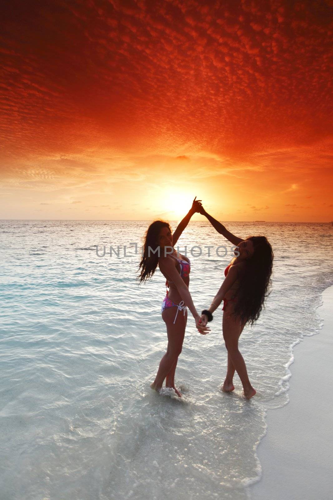 Two beautiful women in bikini enjoying sunset on beach