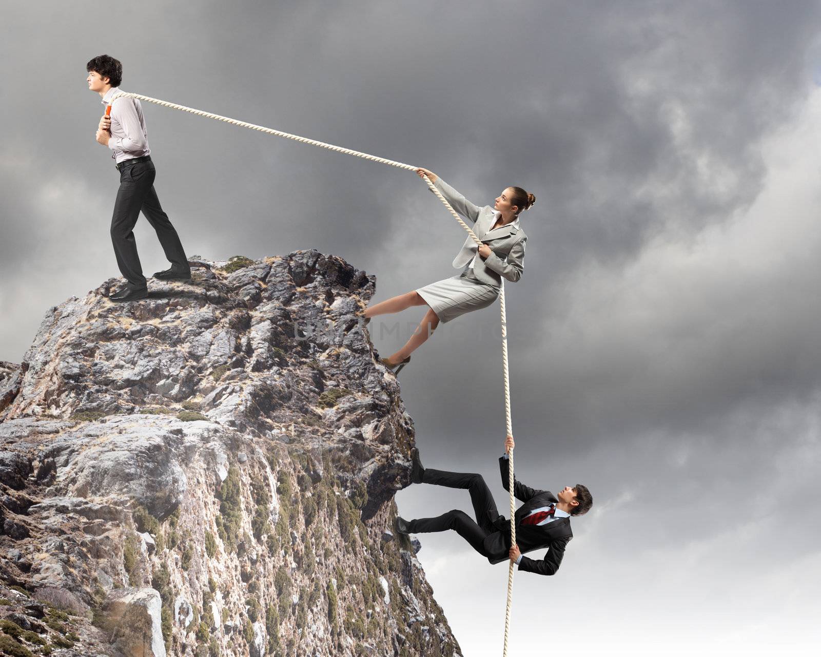 Image of three businesspeople pulling rope atop of mountain