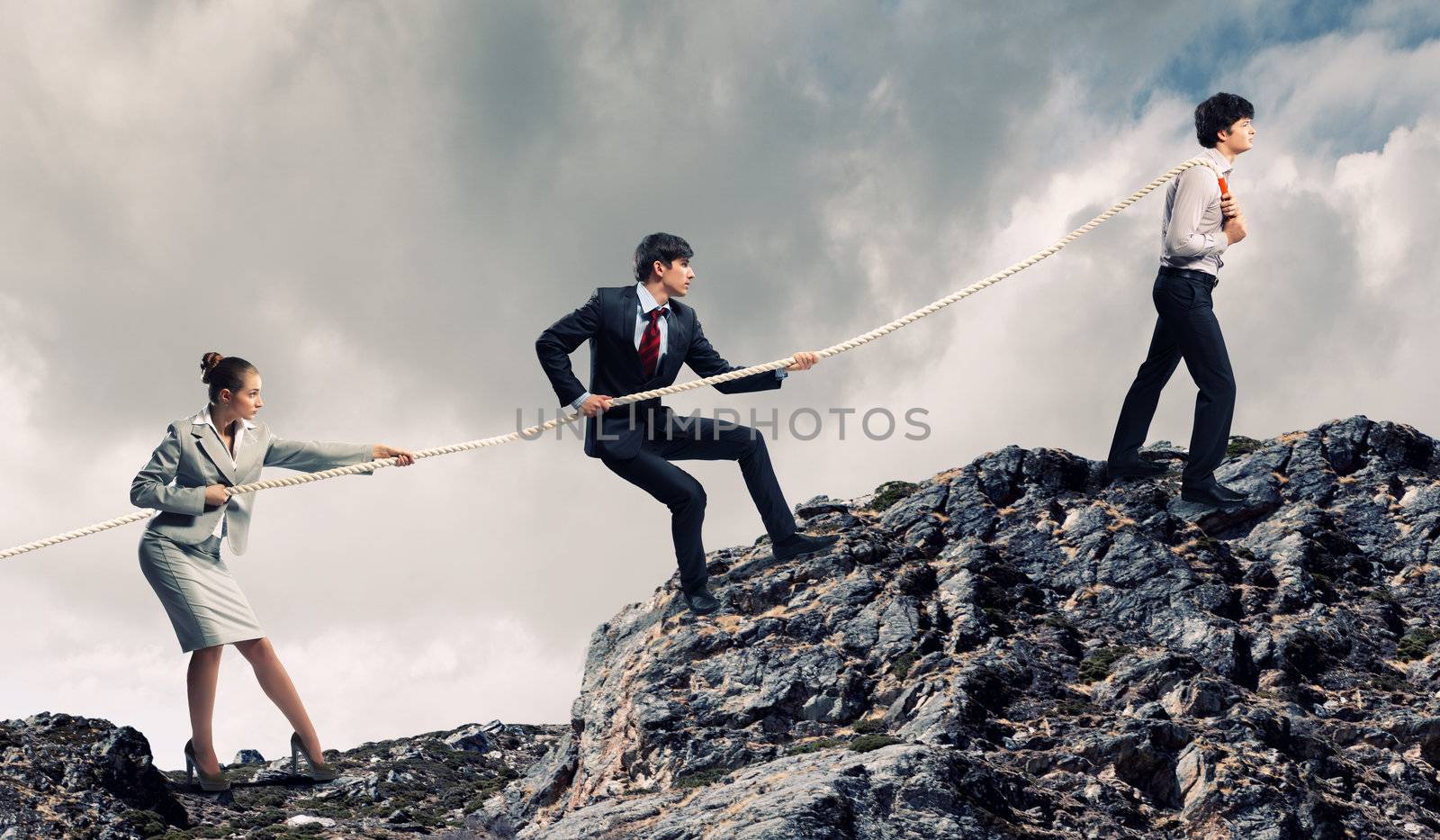 Image of three businesspeople pulling rope atop of mountain