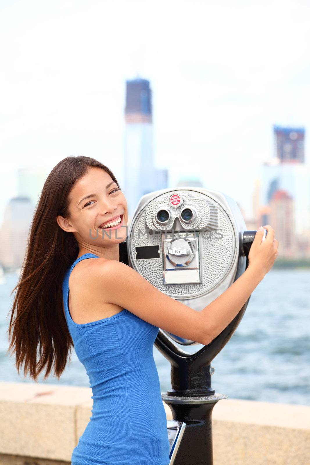 New York tourist woman looking at New York City and Manhattan Skyline in binoculars on Ellis Island. USA tourism concept with multiracial Caucasian / Asian Chinese girl smiling happy in summer.