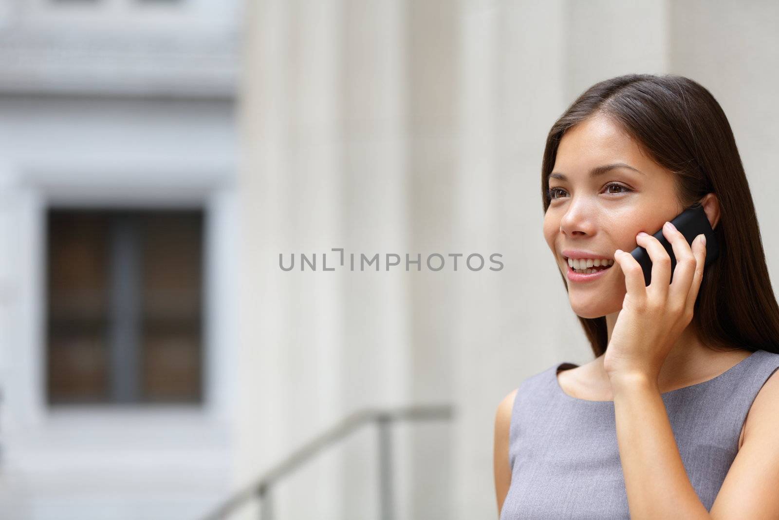 Woman businesswoman lawyer talking on smart-phone outdoors in front of courthouse. Beautiful young mixed race Caucasian / Asian Chinese professional woman.