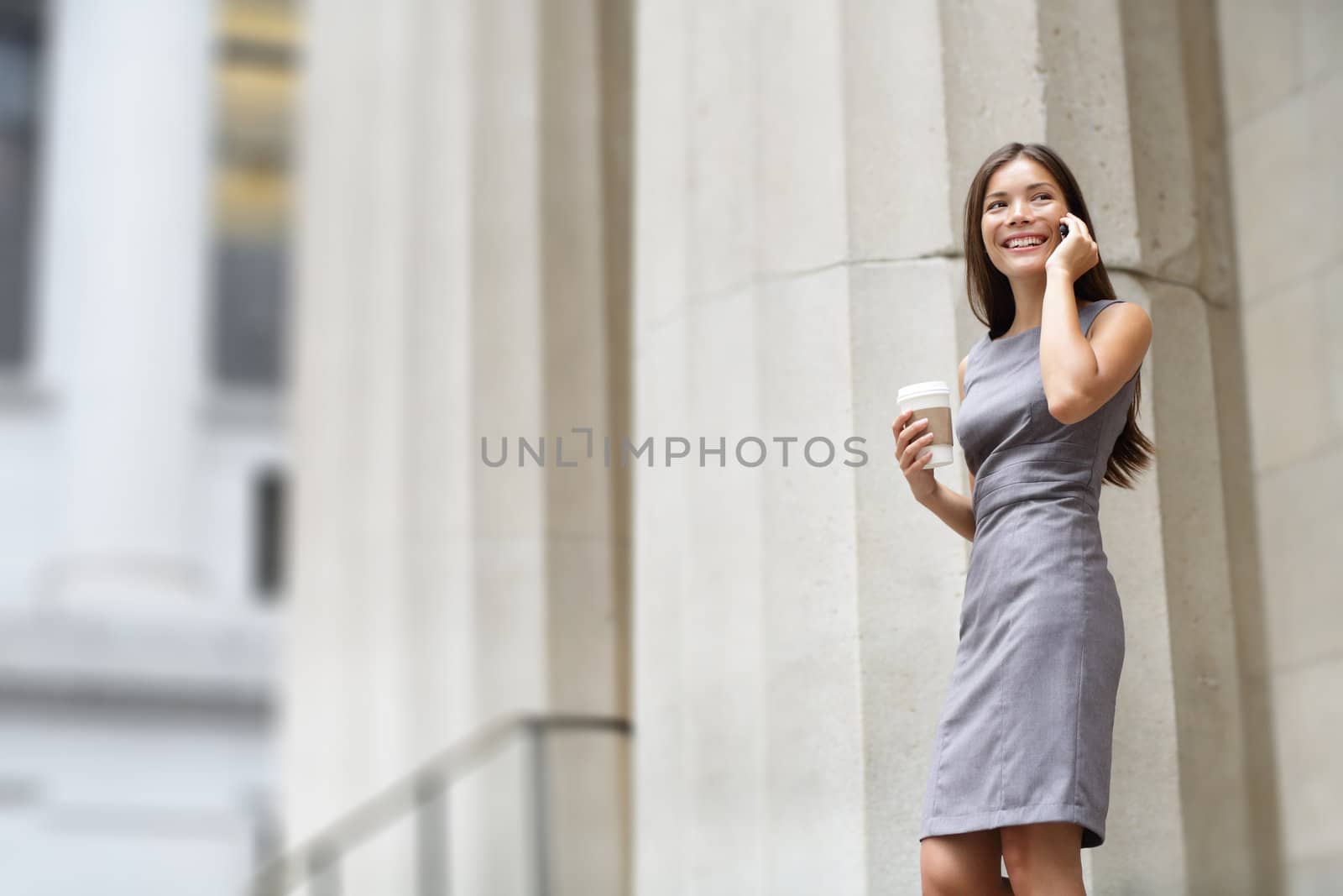 Lawyer businesswoman professional walking outdoors talking on cell smart phone drinking coffee from disposable paper cup. Multiracial Asian / Caucasian businesswoman smiling