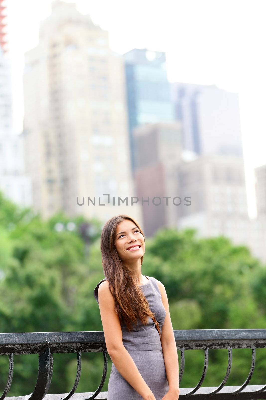 Businesswoman in New York City Central Park standing looking up at copy space with skyscraper buildings from Manhattan skyline in background. Young female professional. Mixed Asian / Caucasian race.