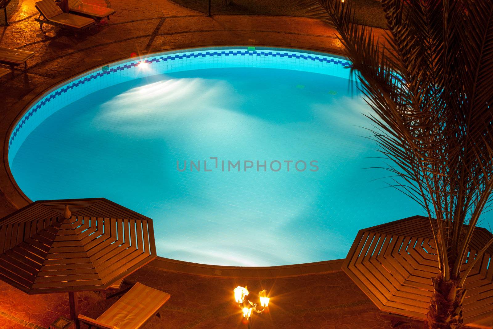 A nighttime view of a luxury villa poolside with umbrellas and tables